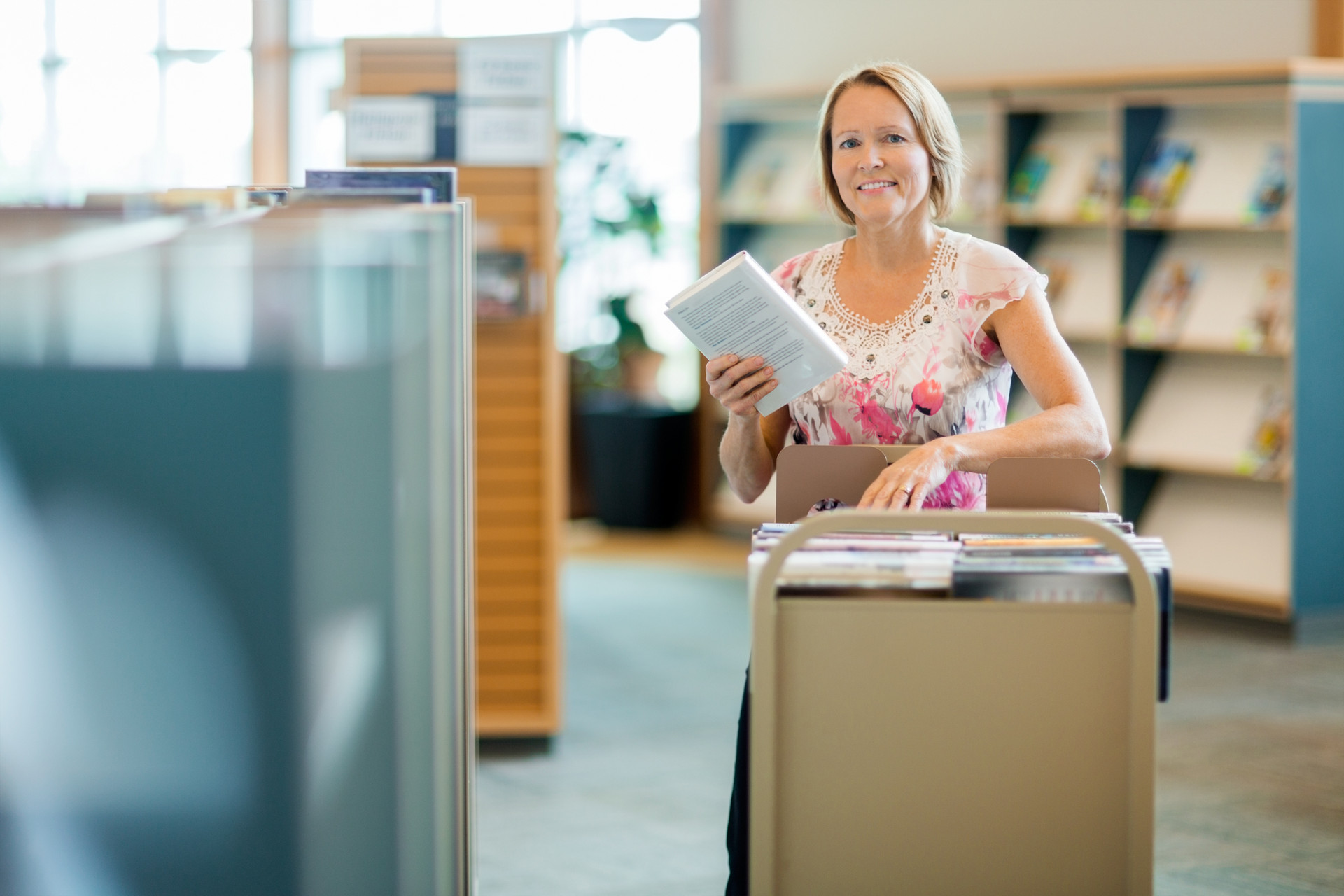 171218027 Portrait of smiling female librarian with trolley of books in library