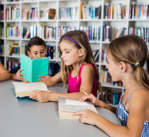 Kinder am Tisch mit Büchern, im Hintergrund Buchregale