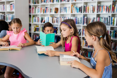 Kinder am Tisch mit Büchern, im Hintergrund Buchregale