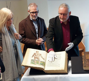 3 Personen stehen um ein historisches Buch herum.