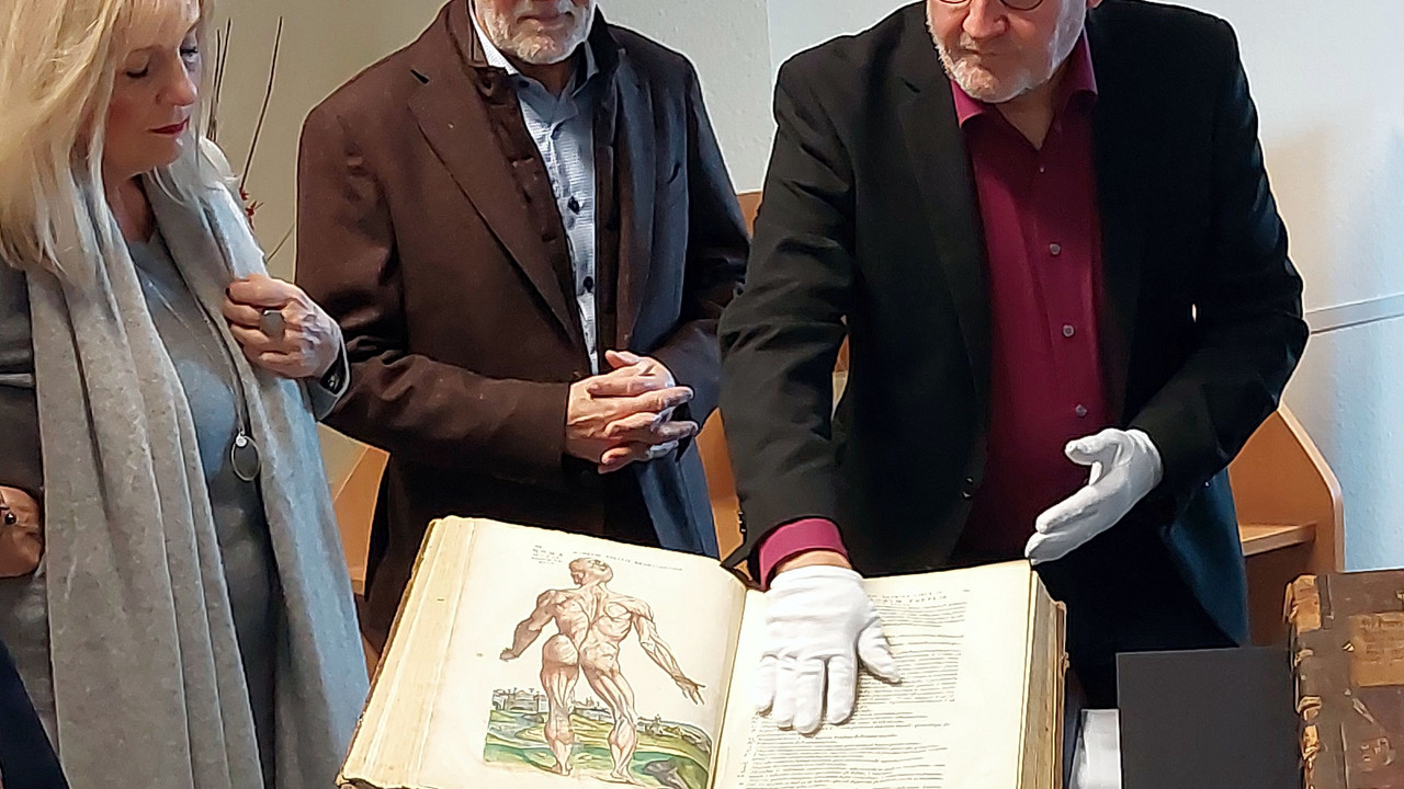 3 Personen stehen um ein historisches Buch herum.