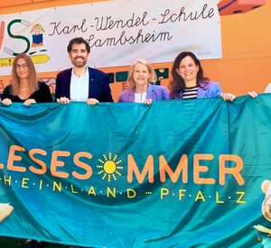 6 Menschen halten eine Stofffahne mit der Aufschrift Lesesommer Rheinland-Pfalz