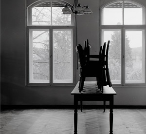 Schwarz-weiß Fotografie, menschenleerer Raum, in der Mitte ein Tisch und hochgestellte Stühle