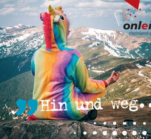 Person in Regenbogenkostüm sitzt im Schneidersitz vor Bergpanorama