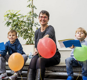 Ute Bahrs sitzt in der Mitte der beiden Gewinnern des Wettbewerbs. All drei halten Luftballons.