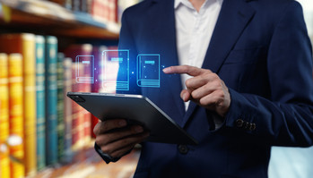 Person mit Tablet in den Händen steht vor Bücherregal