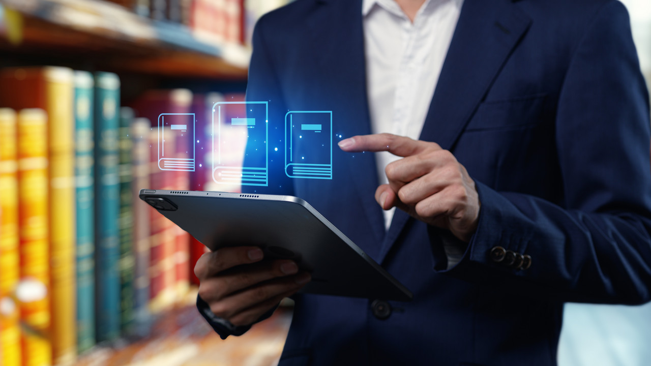 Person mit Tablet in den Händen steht vor Bücherregal