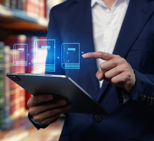 Person mit Tablet in den Händen steht vor Bücherregal