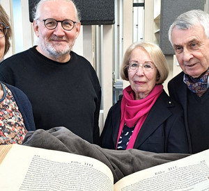 Aufgeschlagenes Buch, dahinter vier Personen