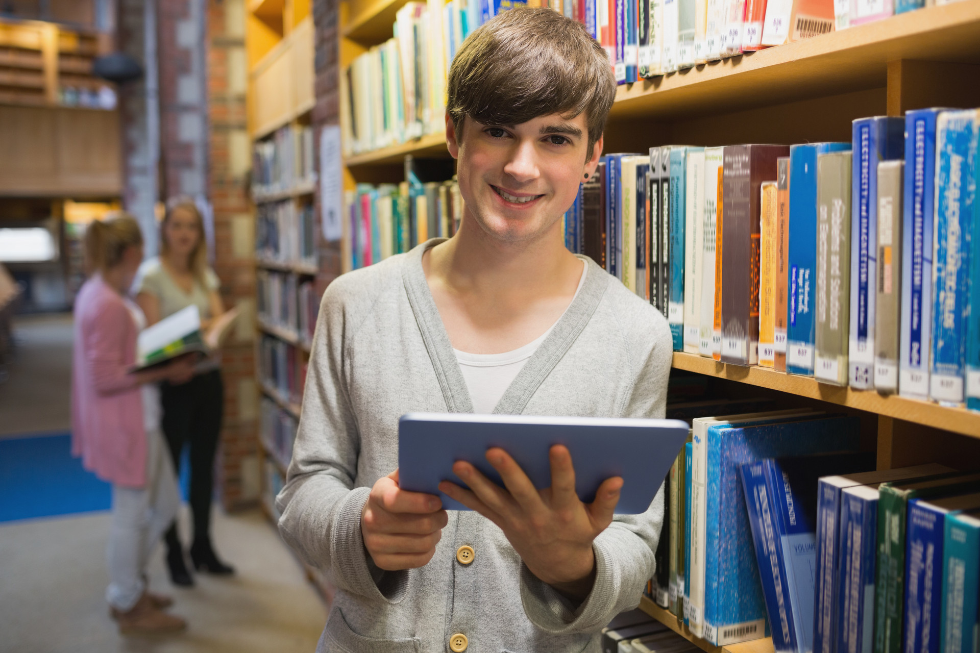 Man standing at a bookshelf holding a tablet pc in college library